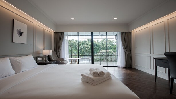 Habitación de hotel con una cama grande, un escritorio, una silla, una mesita y vistas a zonas verdes por las ventanas.