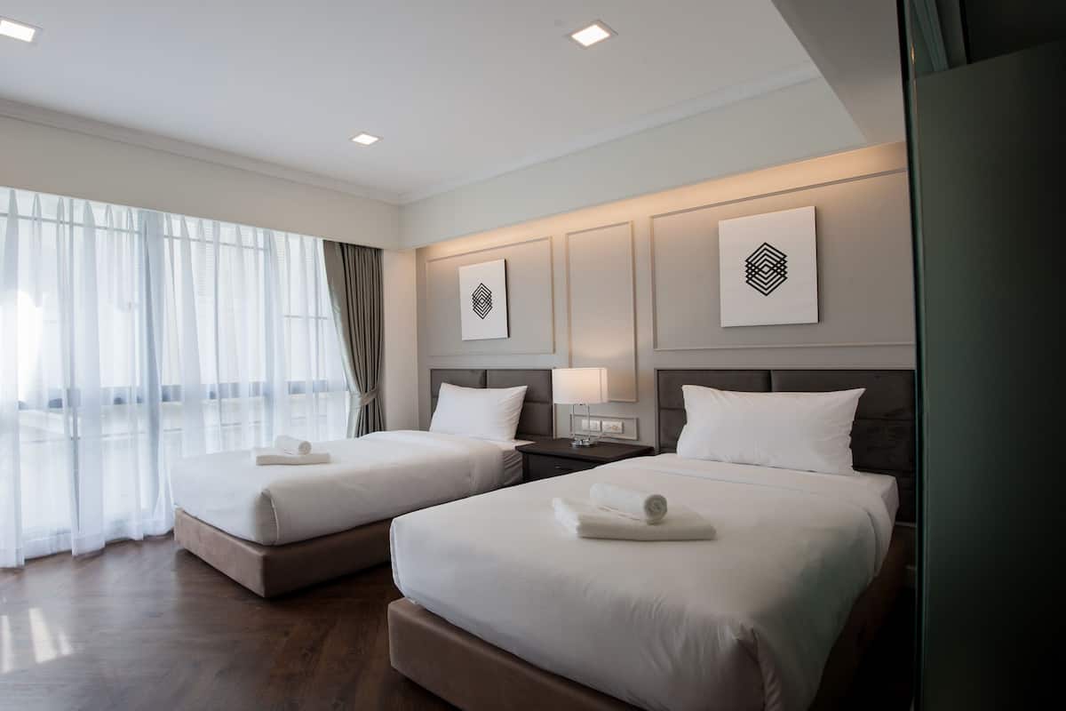 Una habitación de hotel con dos camas, un ventanal con cortinas traslúcidas, una lámpara moderna y obras de arte en las paredes.
