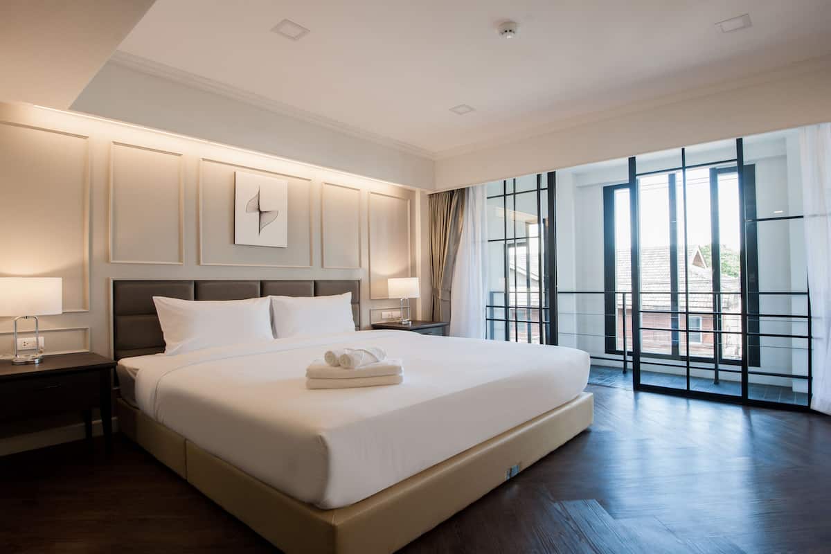 Un dormitorio espacioso con una cama grande, una mesita de noche, una lámpara de pared y vistas a través de ventanales del suelo al techo.