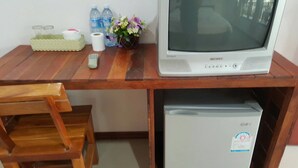 A wooden desk with a Samsung Bilingual CRT TV, a small refrigerator, a remote control, a tissue roll, a glass container, and a vase with flowers. - Sweet Home Chiang Khan (Chiang Khan)