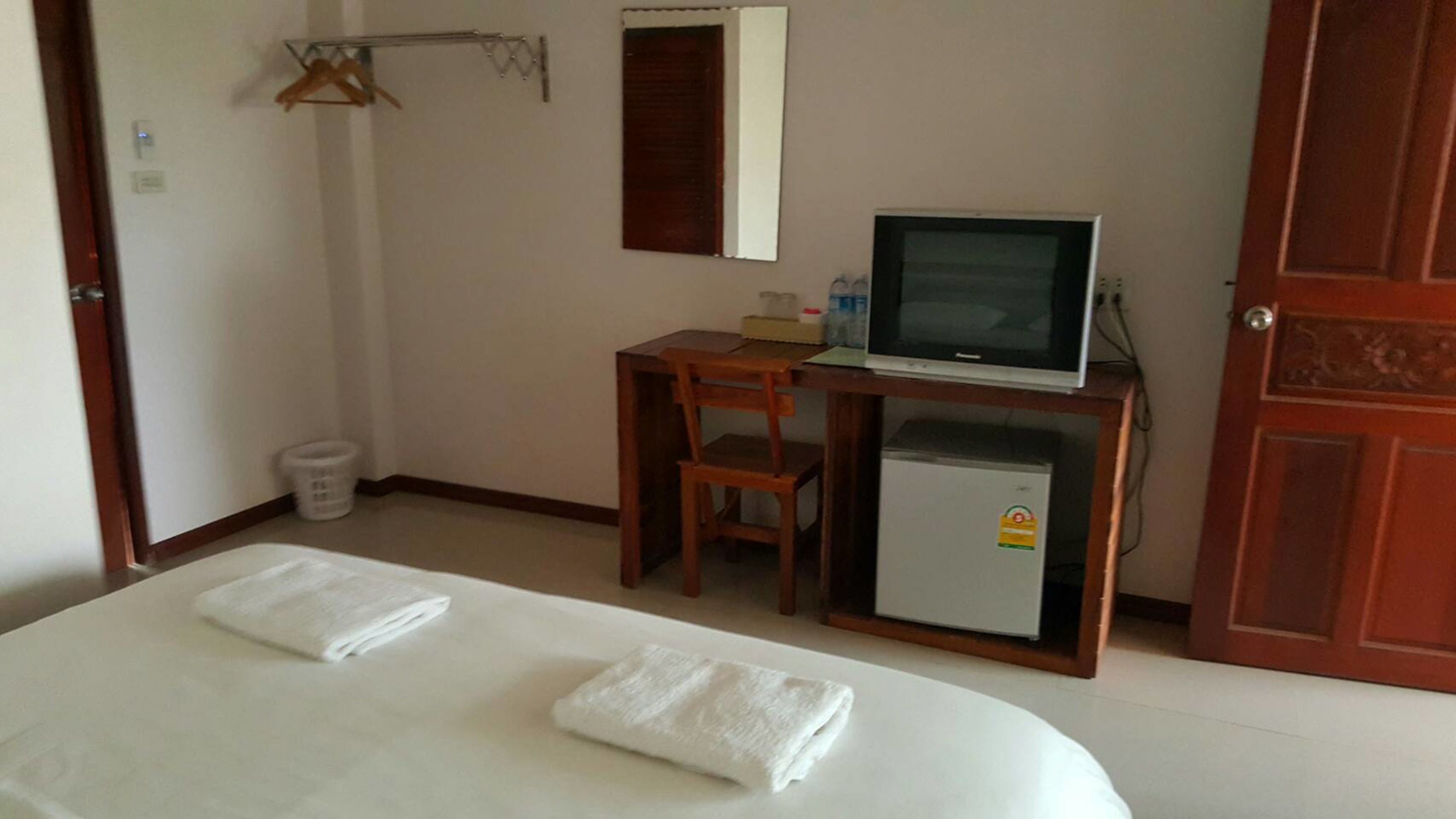 Quarto de hotel com cama, escrivaninha com televisão, um pequeno frigorífico e uma cadeira de madeira.