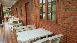 A covered outdoor seating area with white tables and benches, adjacent to a brick building with large windows. - Sweet Home Chiang Khan (Chiang Khan)