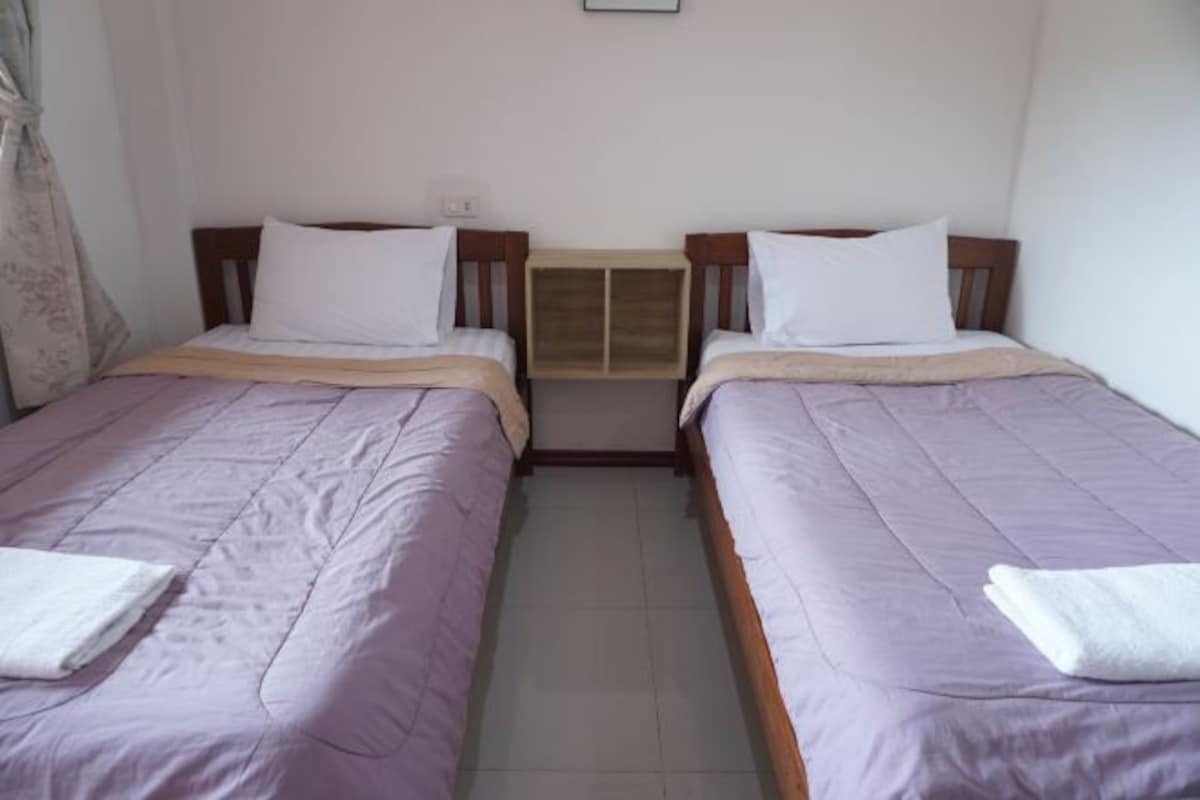 Een kamer met twee eenpersoonsbedden, elk met een houten hoofdbord en witte kussens. Daartussen staat een klein houten nachtkastje.