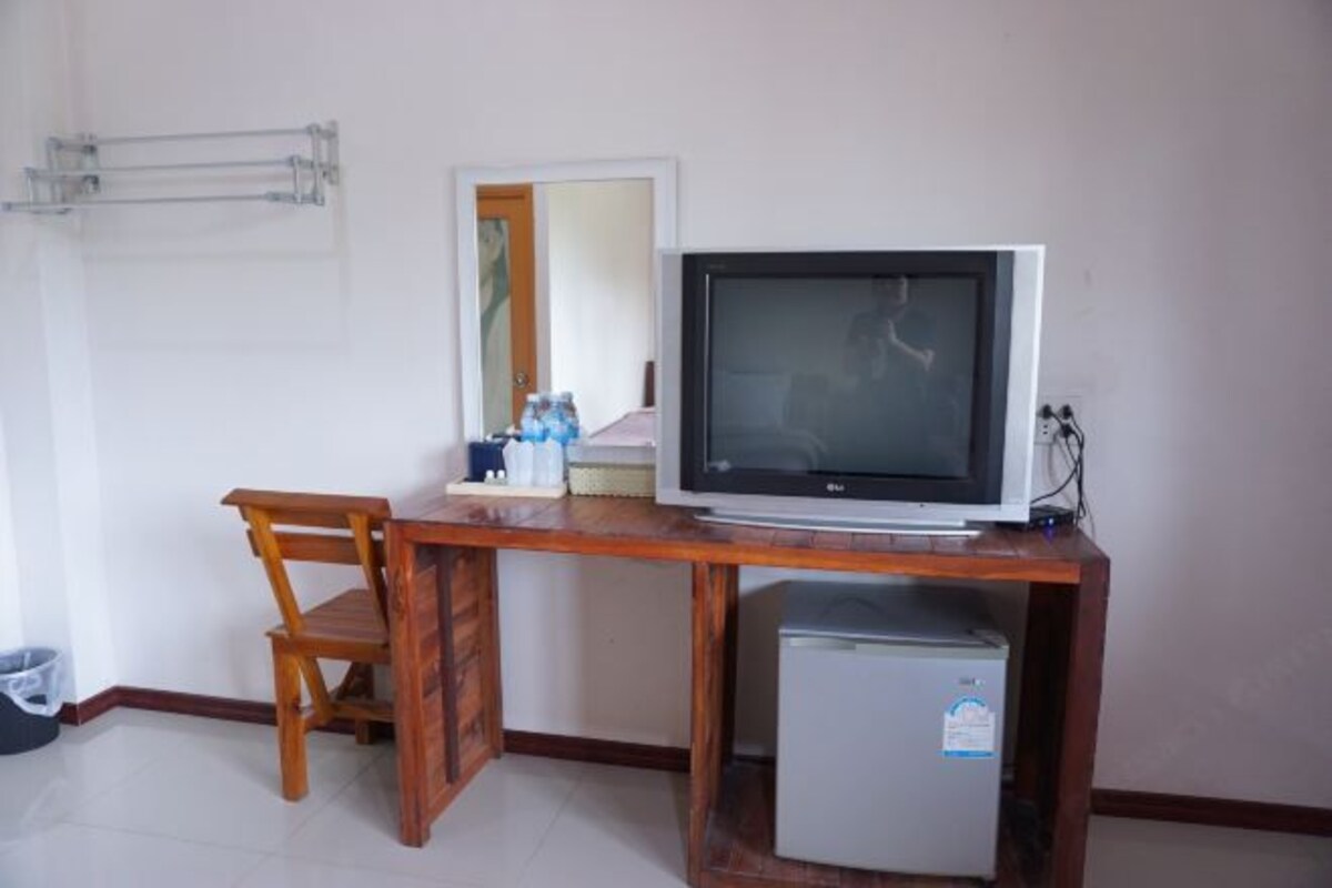 Une pièce de taille modeste, comprenant un bureau en bois, une télévision, un petit réfrigérateur et une chaise.