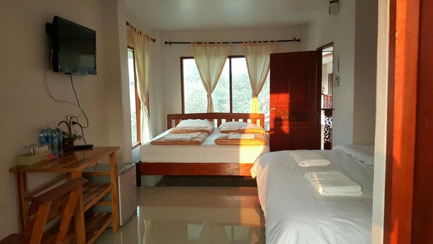 A room with two beds, a wooden desk, a TV mounted on the wall, and a window with curtains. - Sweet Home Chiang Khan (Chiang Khan)