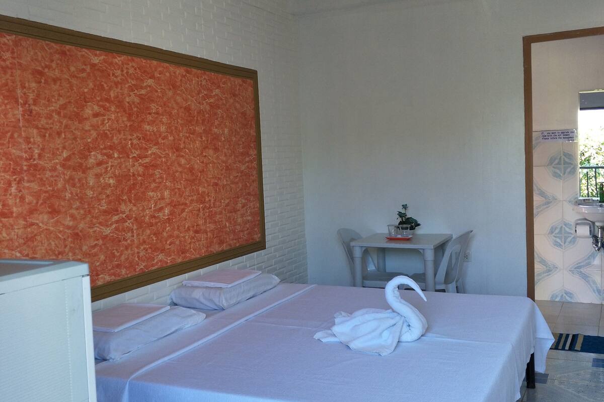 Habitación de hotel con cama, una mesita con silla, televisor y baño visible a través de una puerta abierta.