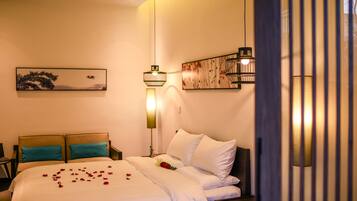 A neatly made bed with white linens and teal pillows, a framed artwork above it, and a bedside table with a lamp.