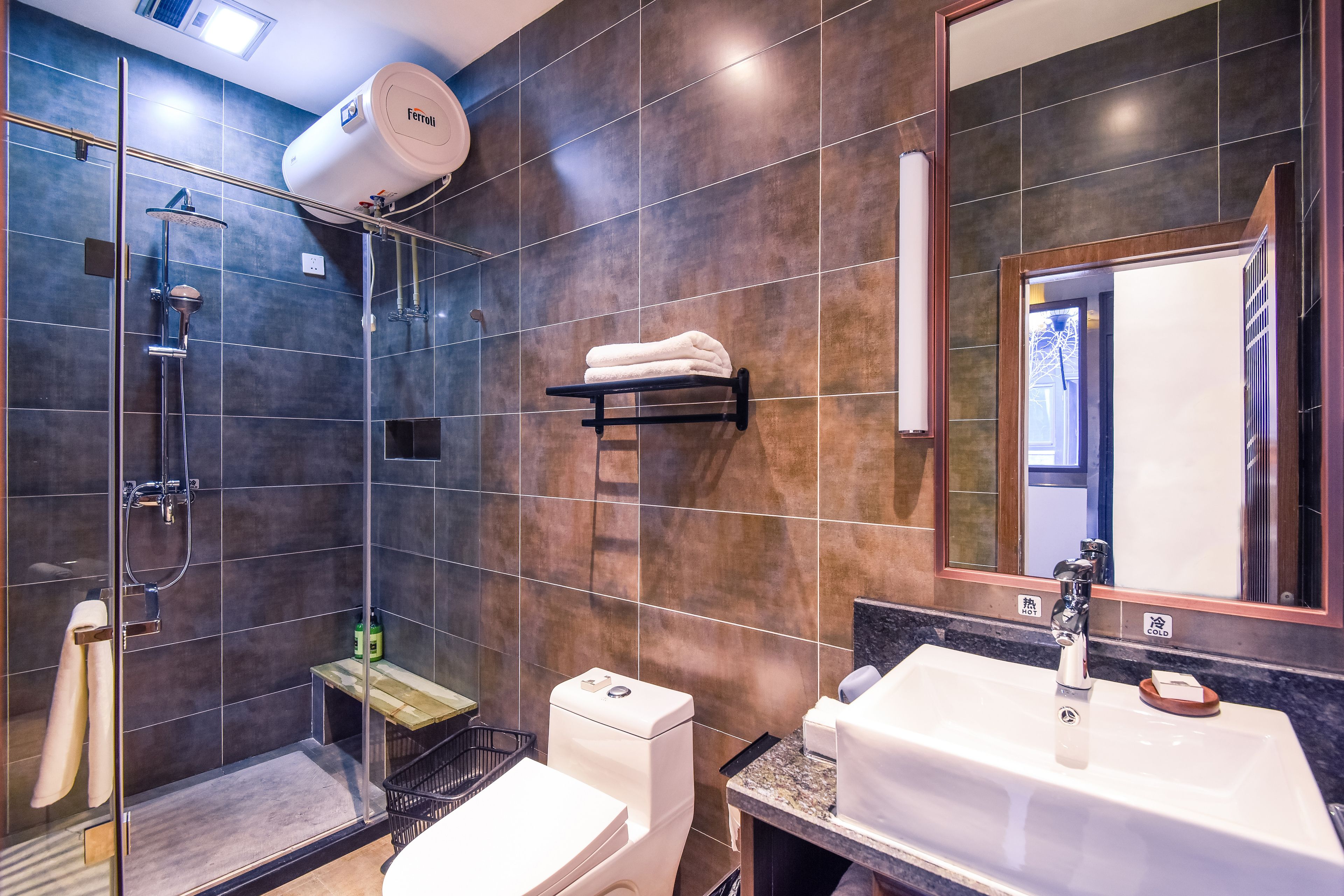 Un baño moderno con ducha envuelta en vidrio, inodoro blanco, lavamanos con espejo y un perchero para toallas.