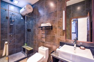 Un baño moderno con ducha envuelta en vidrio, inodoro blanco, lavamanos con espejo y un perchero para toallas.