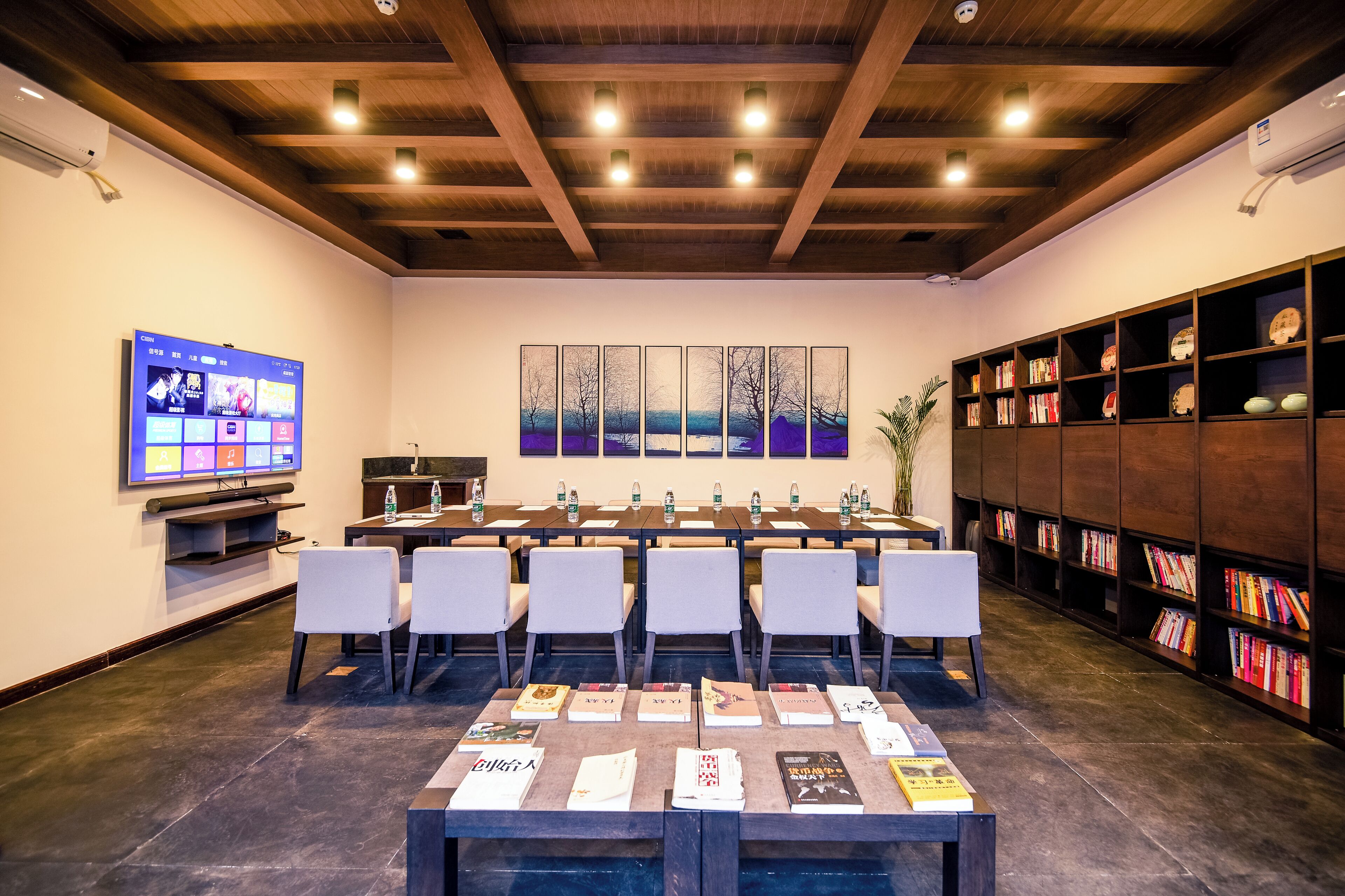 A conference room with a long table, chairs, a television, and bookshelves.
