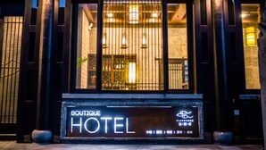 Entrada de um hotel com uma placa indicando "BOUTIQUE HOTEL" e uma vitrine decorativa.