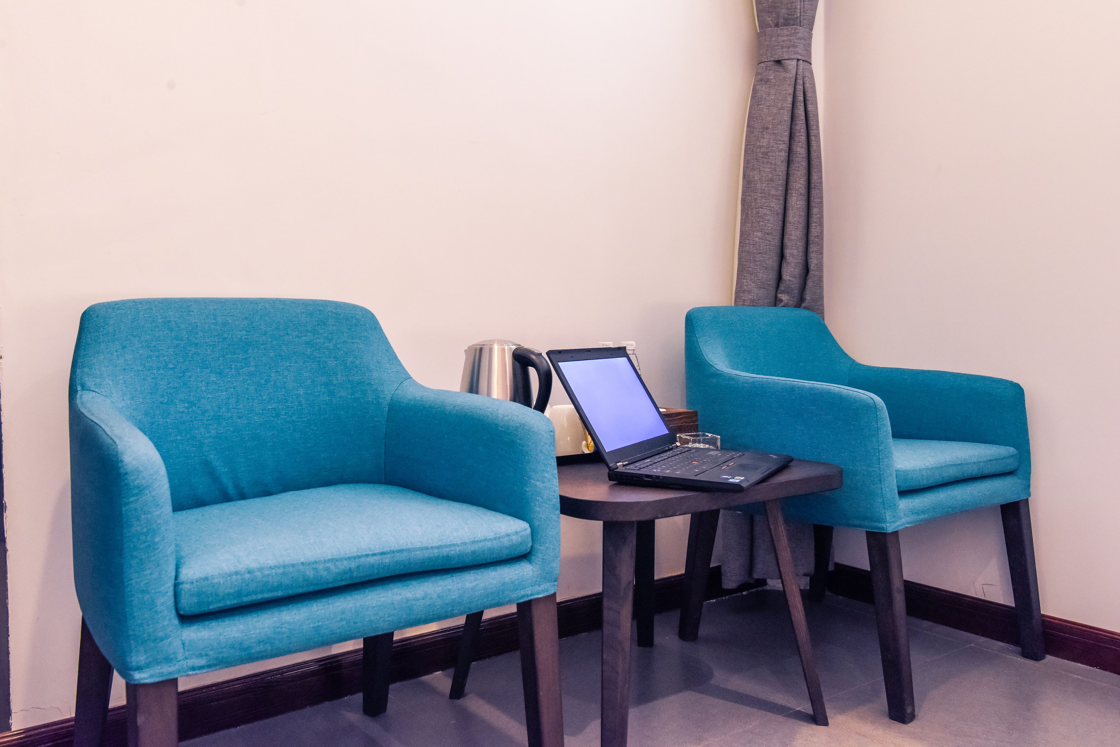 Dos sillones azulados y una mesita con una computadora portátil y un hervidor.
