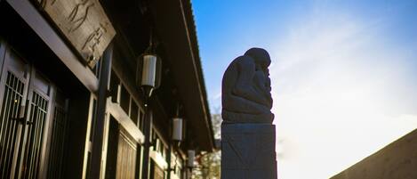 Una estatua de león de piedra frente a un edificio con arquitectura china tradicional, que incluye un tejado de tejas y un farol.