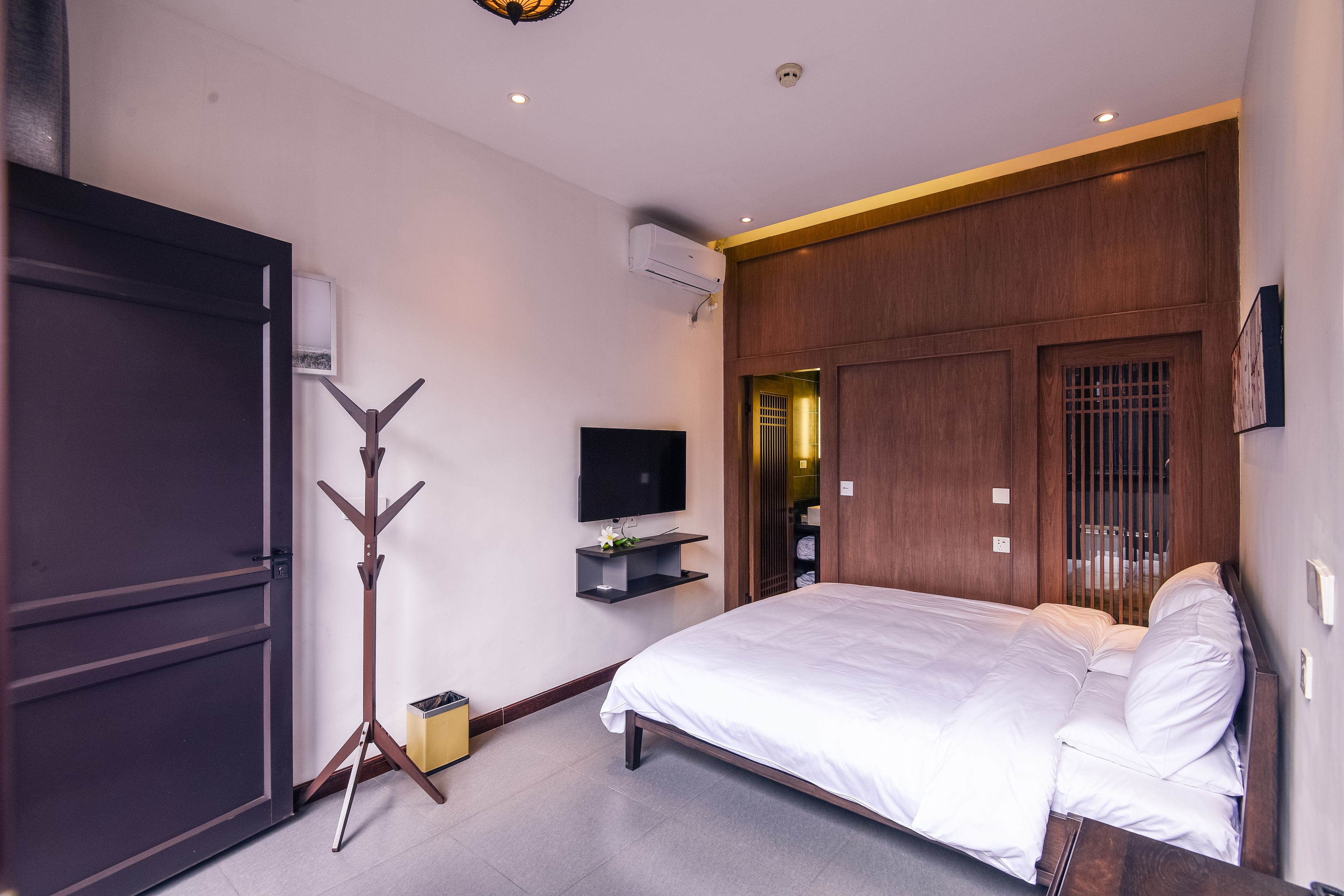 A modern hotel room with a large bed, a flat-screen TV, a coat rack, and a wardrobe.