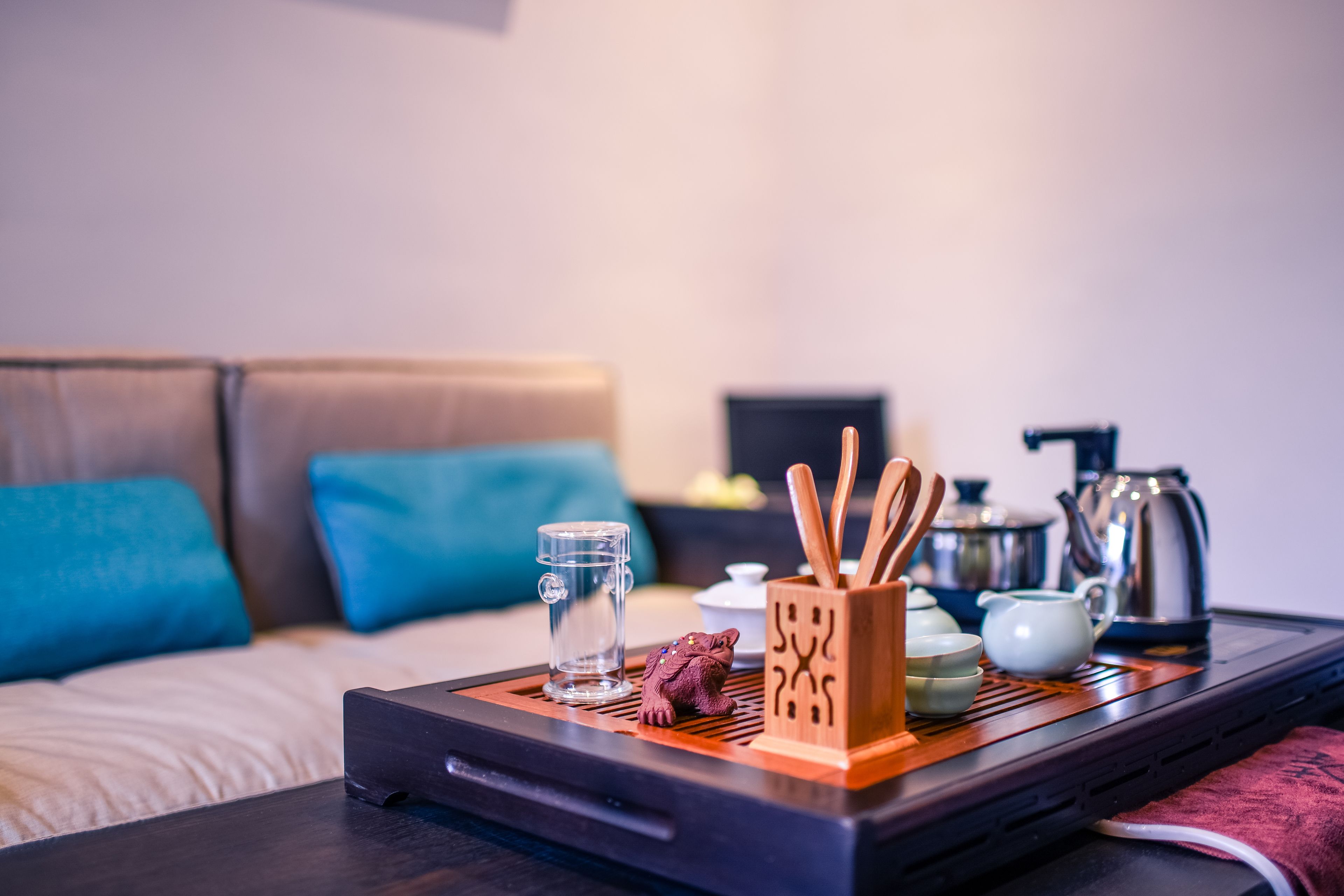 A neatly arranged tray with a teapot, cups, and a decorative frog figurine on a bed with blue pillows.