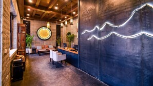 Uma área de recepção com design moderno, incluindo um balcão de atendimento, espaço para assentos e elementos decorativos como um luminária circular e uma parede com padrão de luz ondulado.
