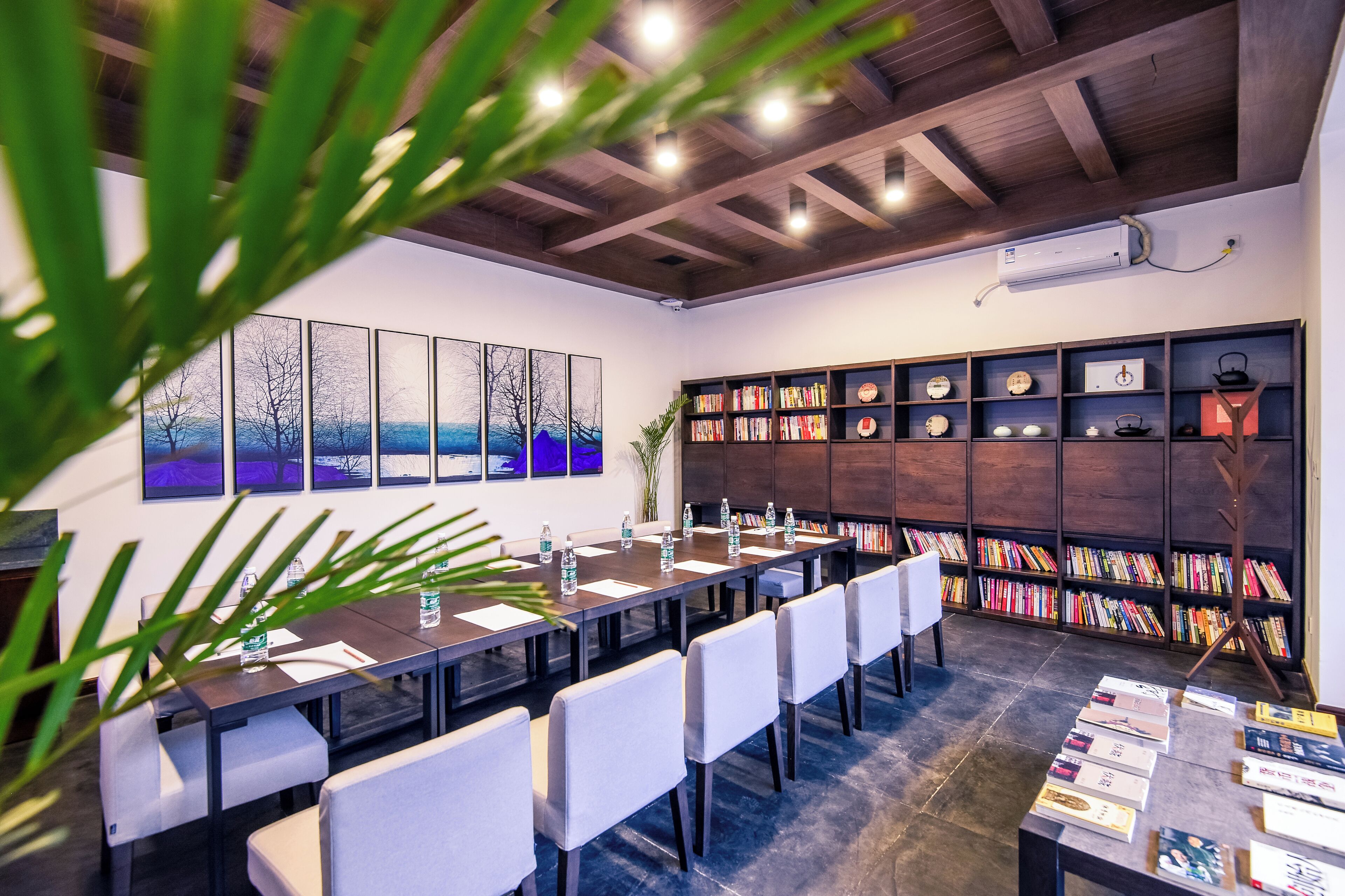 A conference room with a long table, white chairs, and a bookshelf filled with books and decorative items.