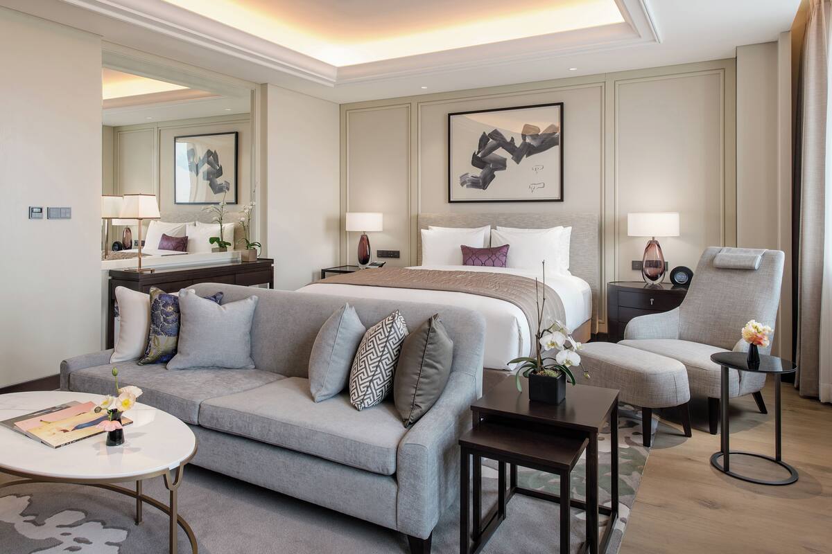A hotel room with a bed, a sofa, a chair, a small table, and a mirror.