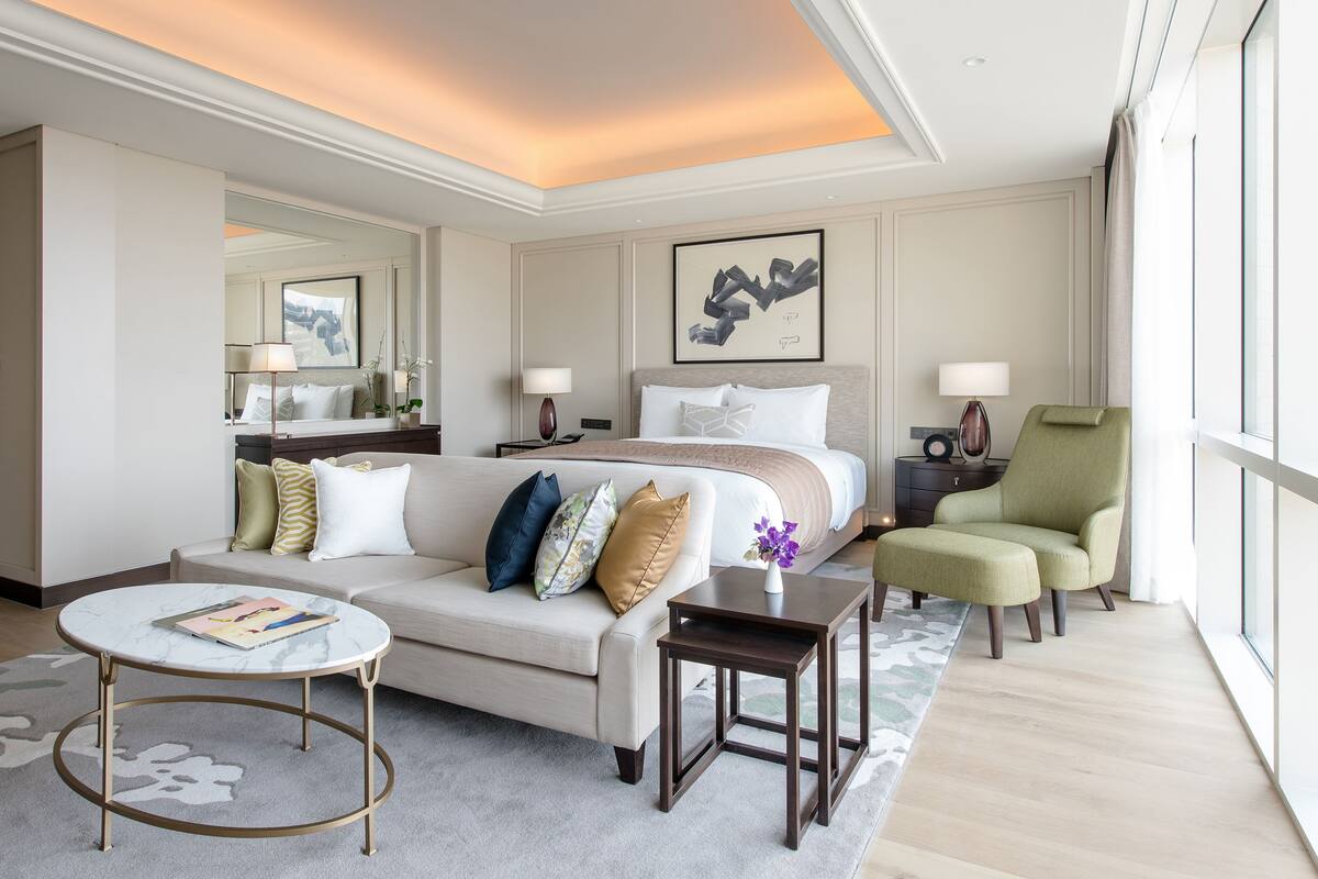 A hotel room with a bed, a sofa, a chair, a small table, and a large window.