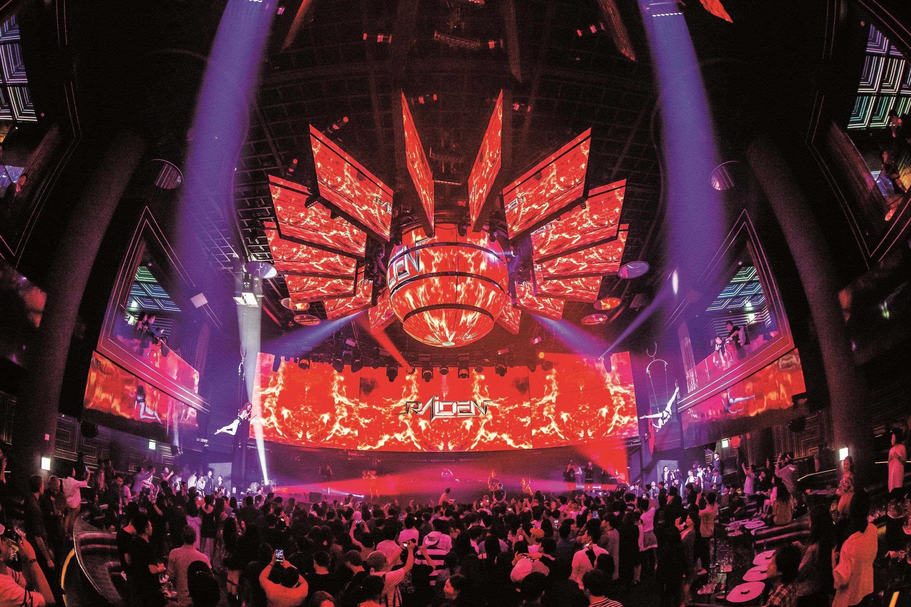 A large indoor venue with a central stage and multiple screens displaying visuals.