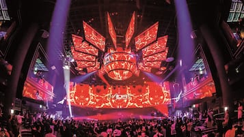 A large indoor venue with a central stage and multiple screens displaying visuals.