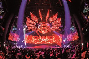 A large indoor venue with a central stage and multiple screens displaying visuals.