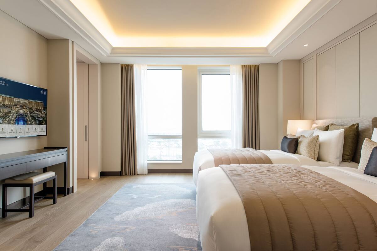 A hotel room with a large bed, a desk, and a view of the outside through a large window.