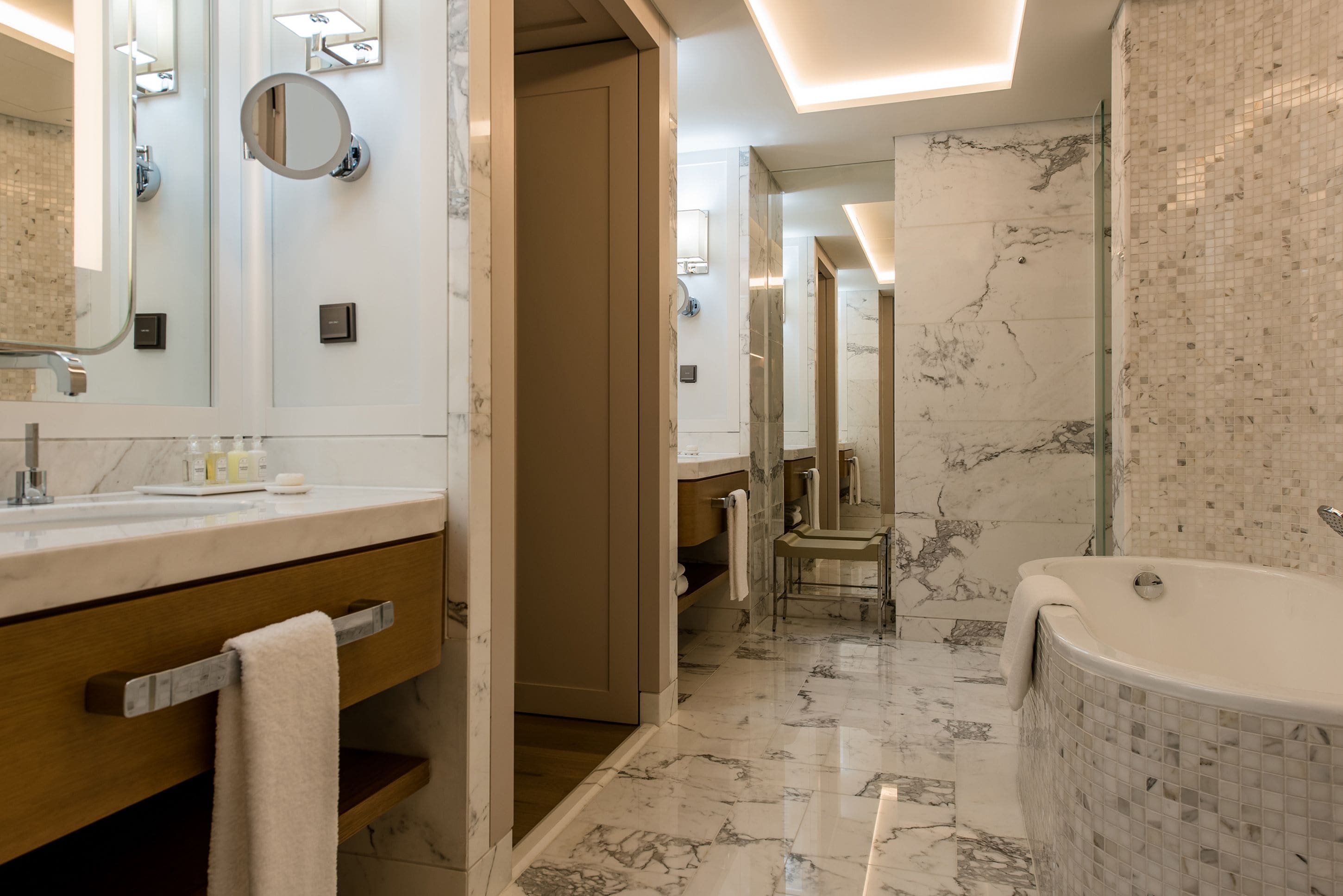 A modern bathroom with a marble floor, a large mirror, a bathtub, and a vanity with a towel rack.