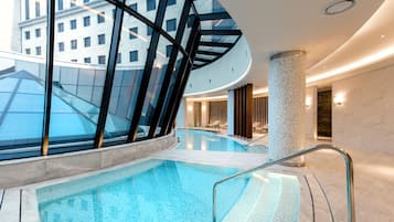 A modern indoor pool with glass walls, a curved ceiling, and a central column.