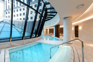 A modern indoor pool with glass walls, a curved ceiling, and a central column.