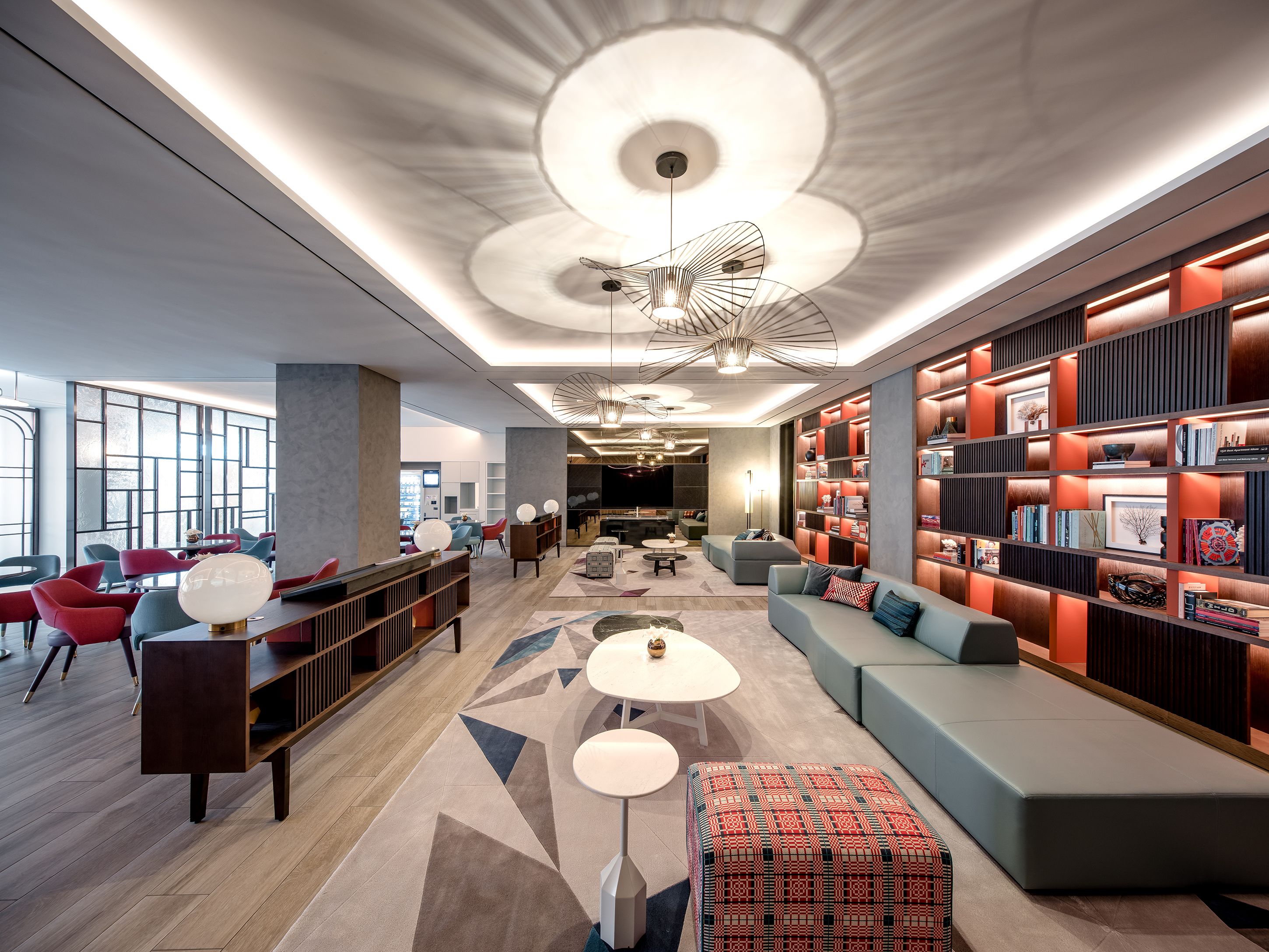 Een moderne lobby met een centraal zitgedeelte, een grote boekenkast en een uniek plafondontwerp.