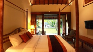 A four-poster bed with a canopy, a bedside table with a lamp, and a view of an outdoor area with chairs and a table. - Adys Inn (Legian)