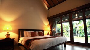 A hotel room with a large bed, two bedside lamps, and a view of a garden through a sliding glass door. - Adys Inn (Legian)