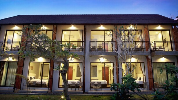 A two-story building with large windows and balconies, featuring multiple rooms with beds and seating areas. - Adys Inn (Legian)