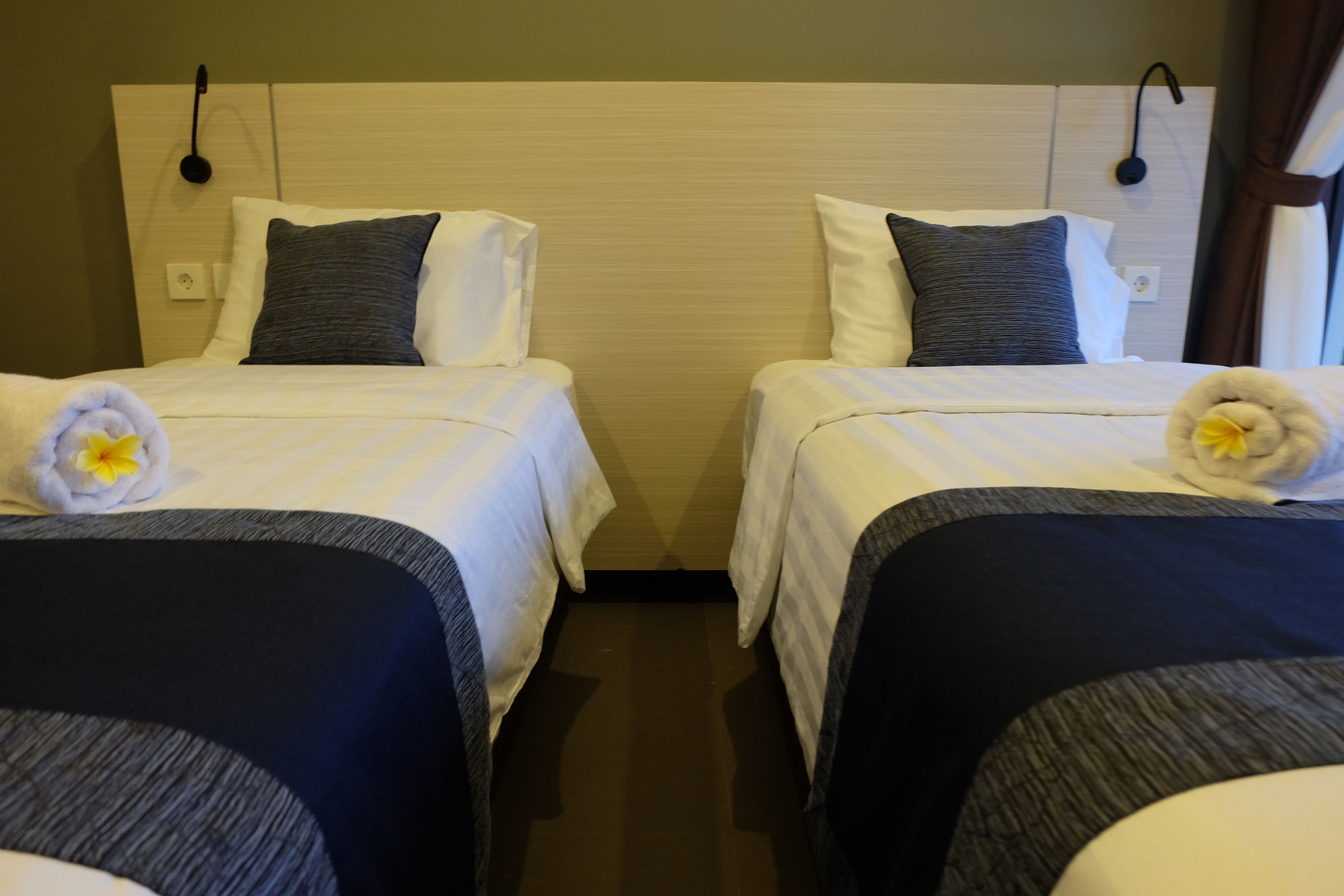 Twin beds with white and dark bedding, a wooden headboard, and a small flower on each bed.