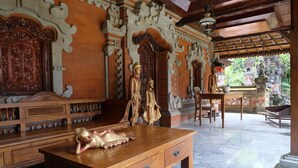 A traditional wooden bench with intricate carvings, a wooden table with a statue, and a stone balustrade. - Adys Inn (Legian)