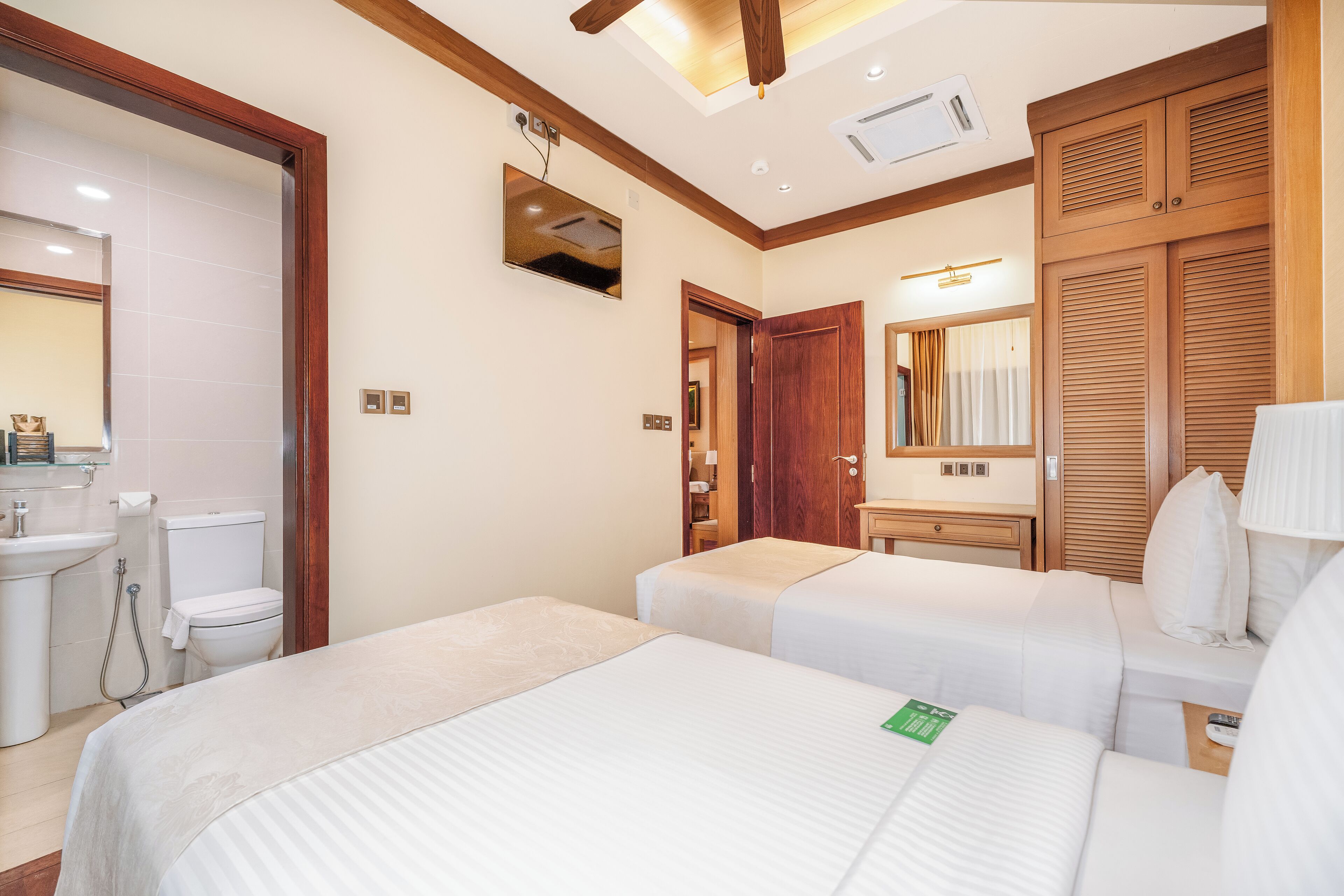 A hotel room with two beds, a bathroom, a wooden wardrobe, and a mirror.
