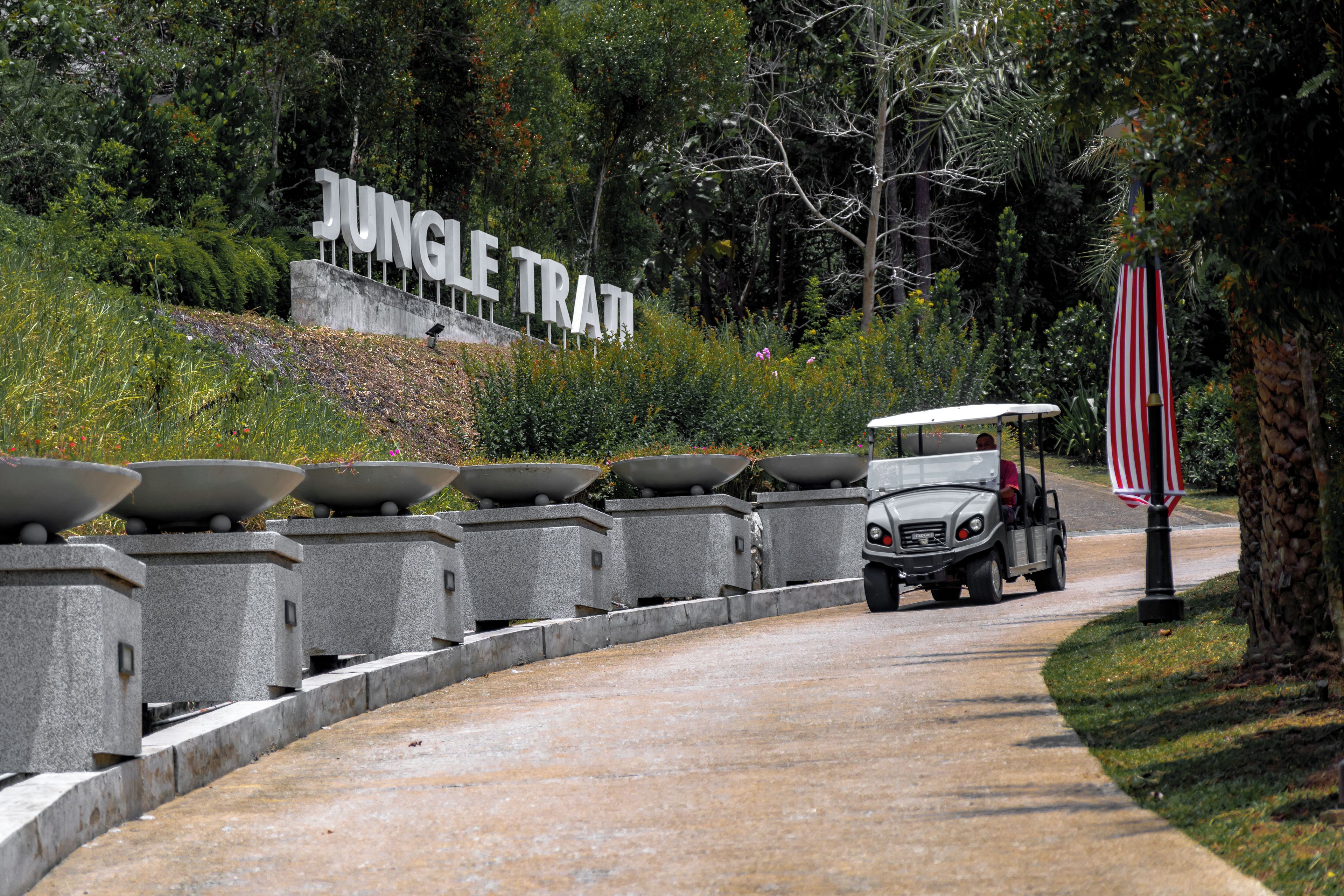 Un sendero que lleva a un cartel que dice 'Jungle Trail', con un carrito de golf estacionado a un lado.