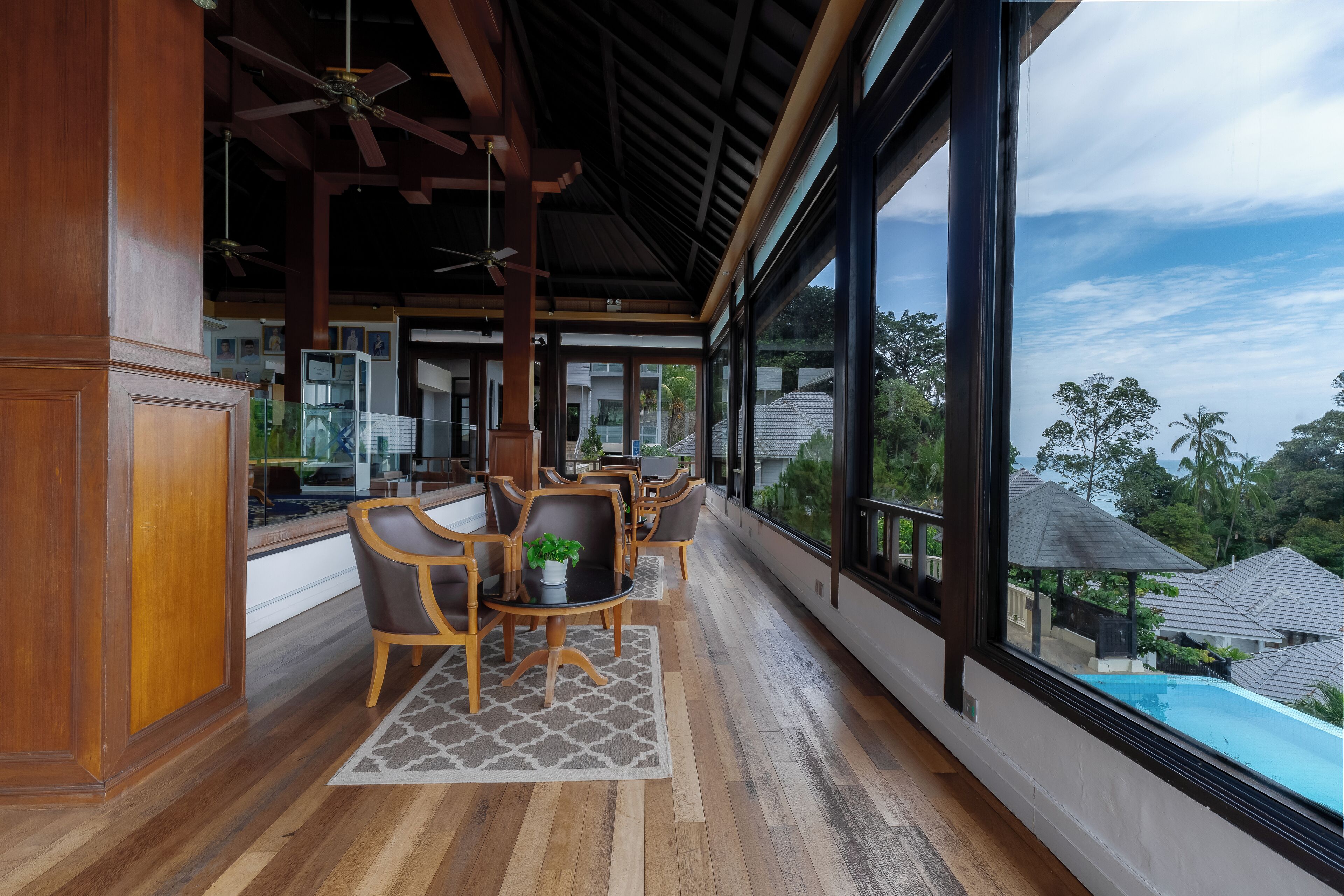 A spacious balcony with wooden flooring, a dining area with chairs and a table, and large windows offering a view of the surrounding neighborhood.