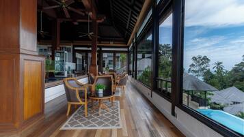 A spacious balcony with wooden flooring, a dining area with chairs and a table, and large windows offering a view of the surrounding neighborhood.