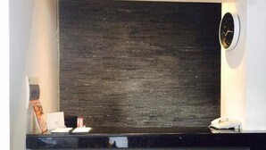 A reception desk with a dark textured wall, a clock, and a phone on the counter.