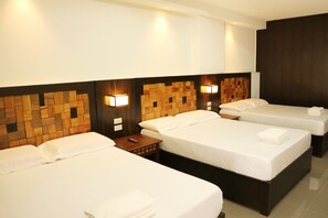 A hotel room with three beds, wooden headboards, and wall-mounted lights. - West Gate Hotel (Laoag)