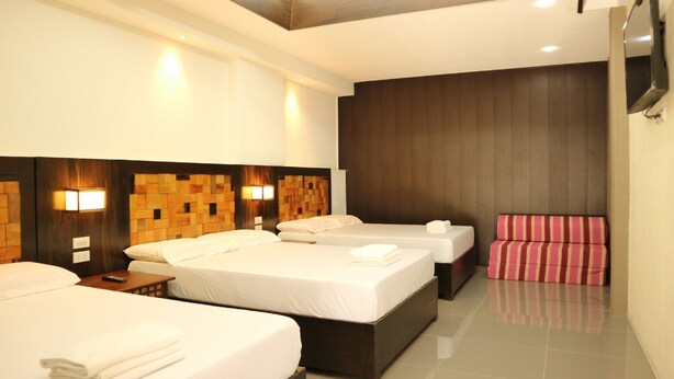 A hotel room with three beds, a flat-screen TV, a wooden headboard, and a tiled floor.