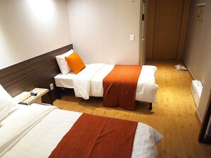 Habitación de hotel con dos camas, cada una con ropa blanca y detalles naranja.