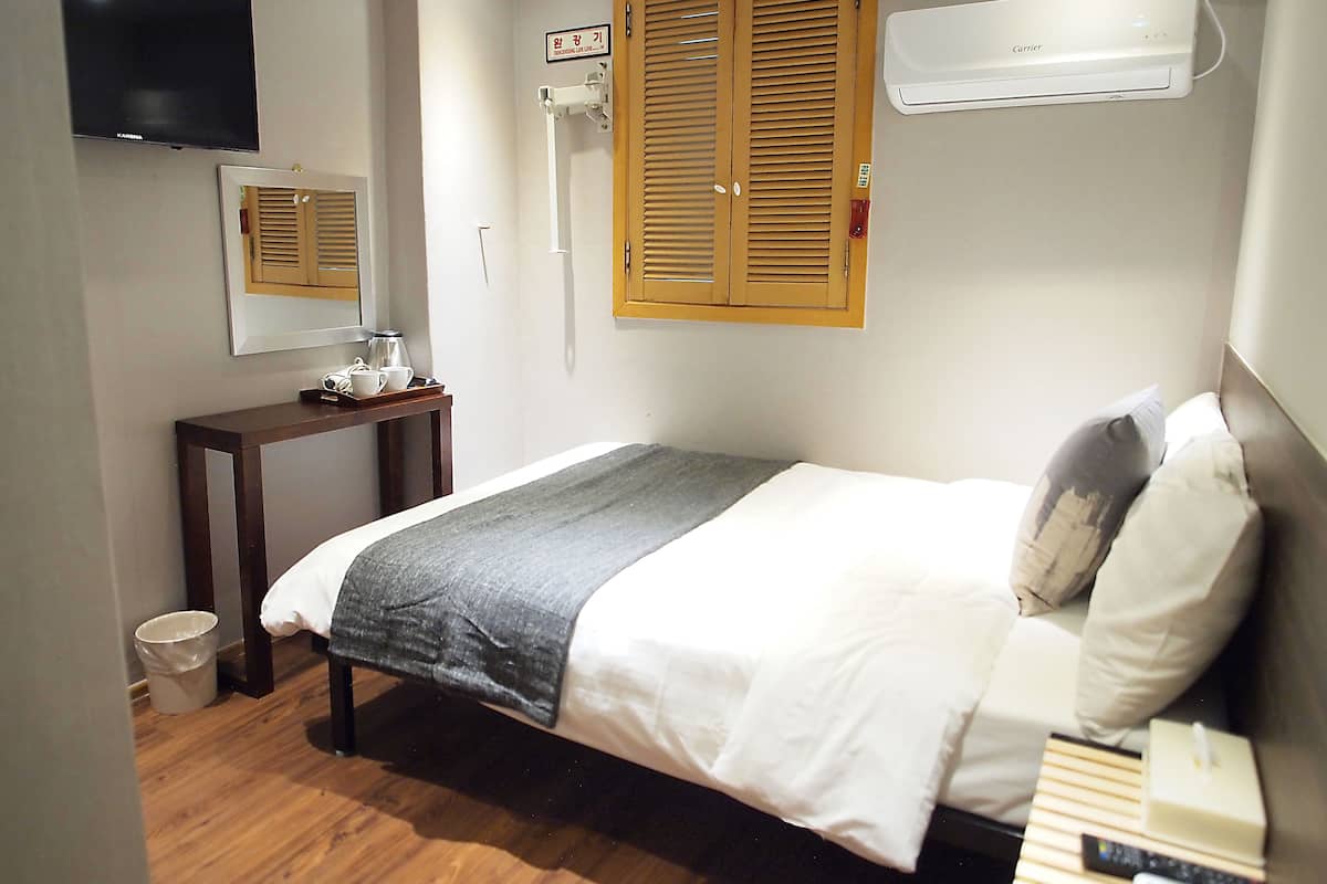 Un dormitorio con cama, mesita de noche, espejo y televisor montado en la pared.