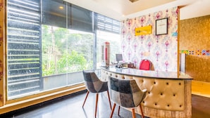 A reception desk with a computer, a red chair, and a large window with blinds. - FabHotel VJR HSR (Bengaluru)