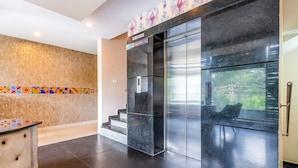 A modern lobby with a marble staircase, a no-smoking sign, and a view of greenery through the elevator doors. - FabHotel VJR HSR (Bengaluru)
