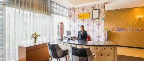 A hotel reception area with a receptionist, a counter, and two chairs.