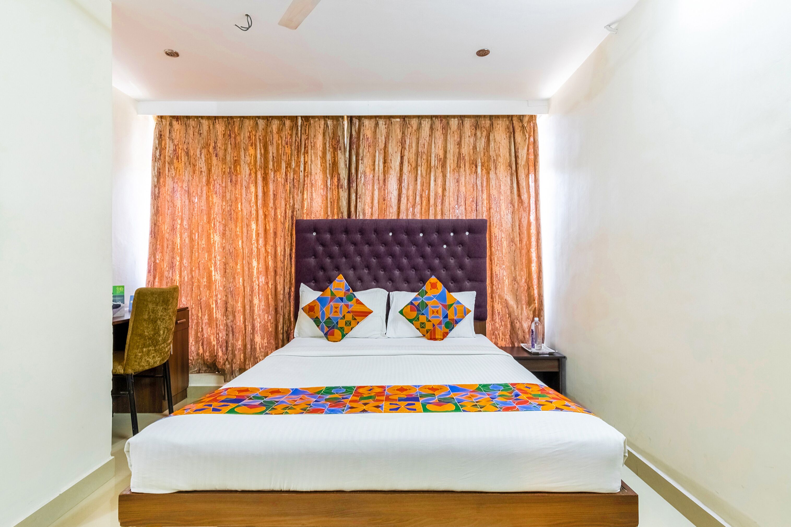 A neatly made bed with a tufted headboard, a colorful bedspread, and two decorative pillows.