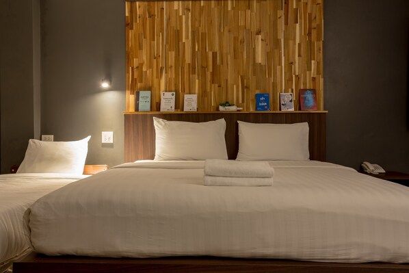 Una habitación de hotel con una cama grande, dos almohadas, una mesita de noche, un cabecero de madera con objetos enmarcados y un buró con un teléfono.